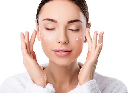 Beautiful middle-aged woman applying skin care product like the prescription grade skin care products sold at White Mountain Med Spa in NH.