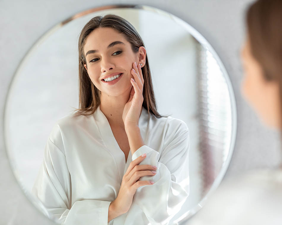 Beautiful young-looking middle-aged woman looking in the mirror and smiling.